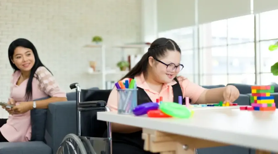 Young woman in a wheelchair building skills with colourful blocks while a support worker watches